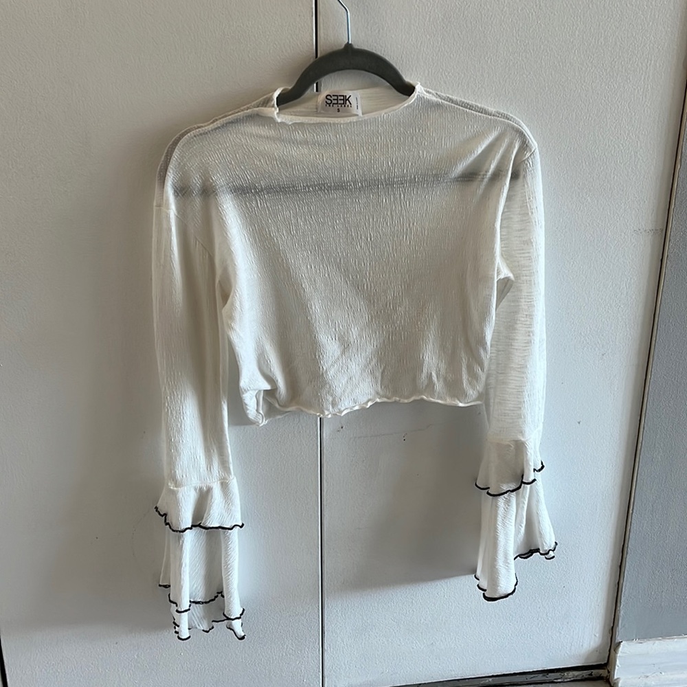 White blouse with bell sleeves and black stitching.